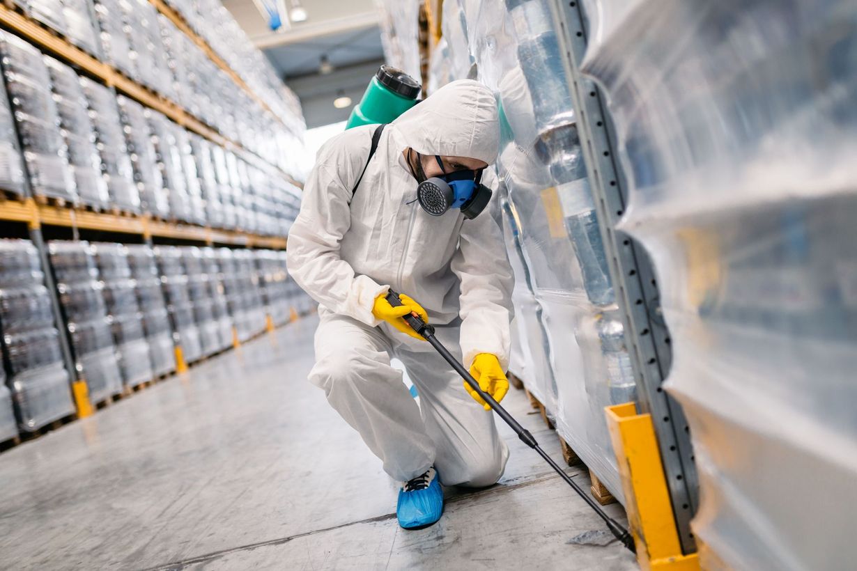 Worker in white protective suit cleaning a warehouse aisle with a yellow pressure washer