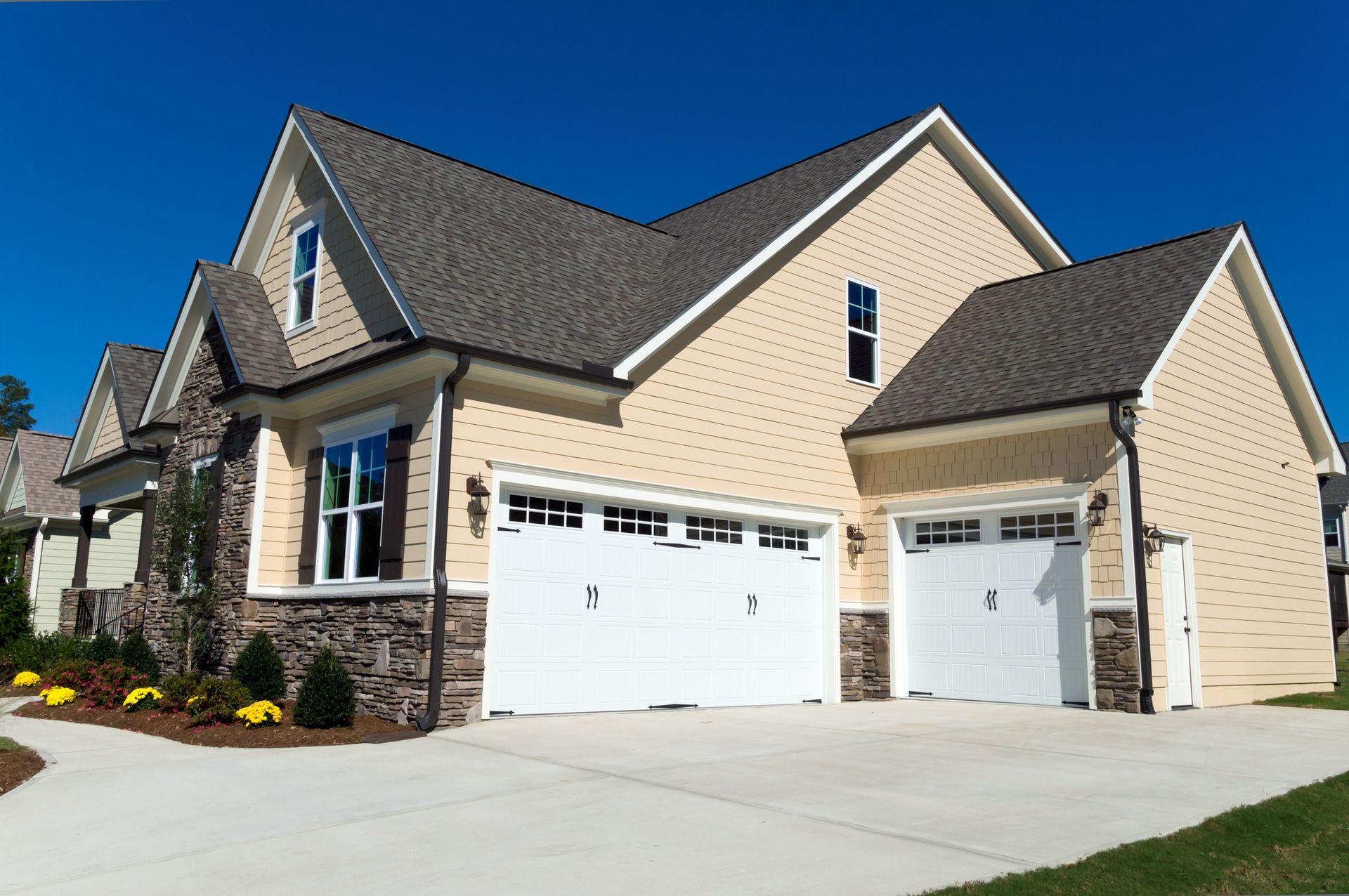 Tan house with two-car garage, stone accents, and blue sky.