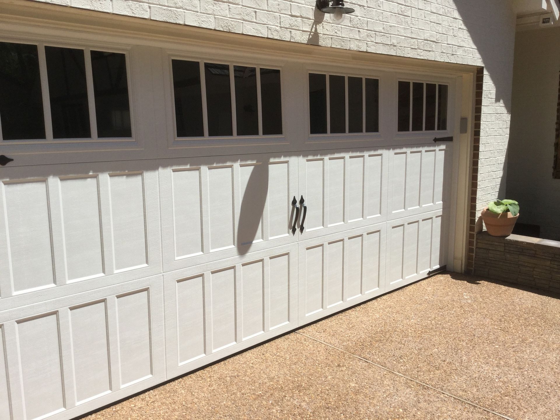 White garage door with rectangular windows at the top, set against a brick wall.