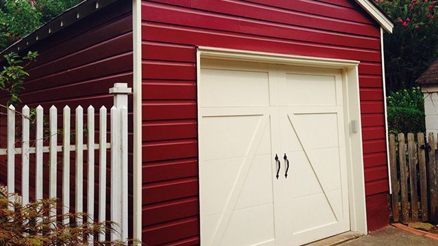 Red shed with white door and trim, next to a white picket fence.
