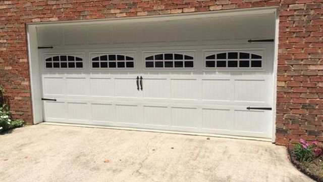 White garage door with arched windows, black hardware, and brick wall exterior.