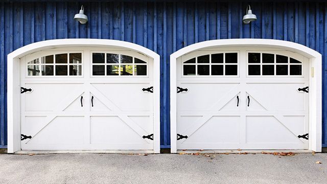 Two white arched garage doors with black hardware against a blue wooden wall.