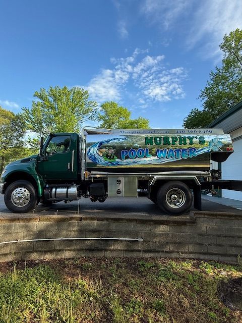 A green water truck is parked in front of a house.