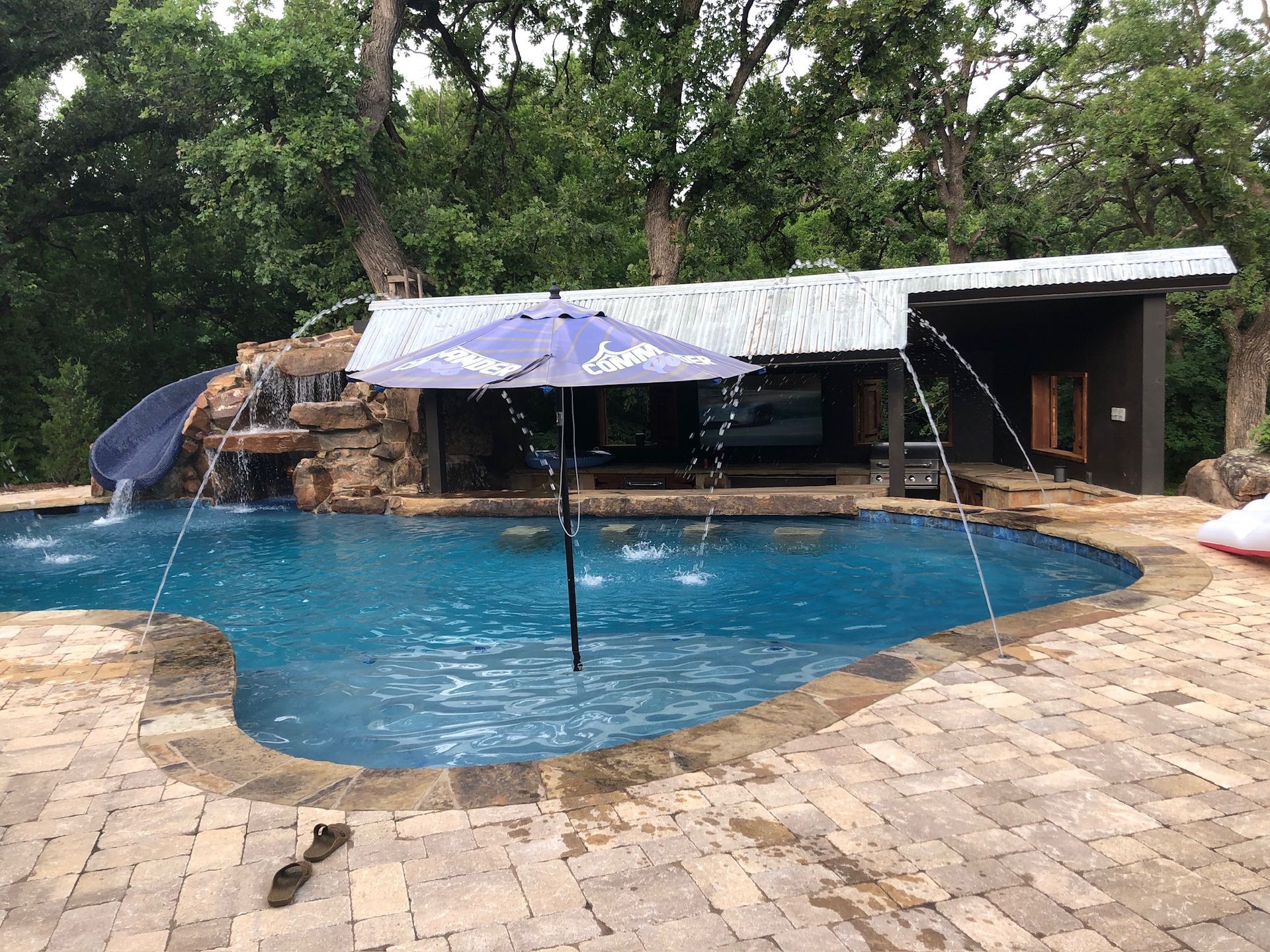 a large swimming pool with a purple umbrella and a water slide