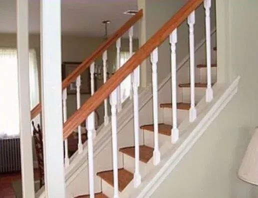 Wooden staircase with white spindles, brown handrails, and tan steps.