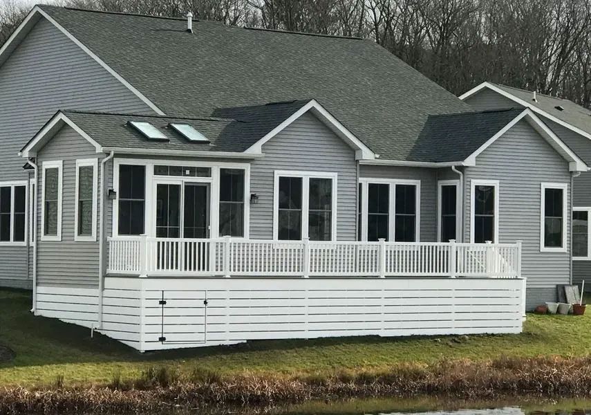 White deck and sunroom addition on a gray house with a pond in the foreground.
