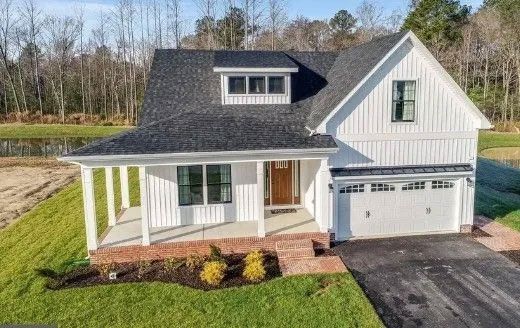 White farmhouse with porch and garage, set on green lawn with trees in the background.