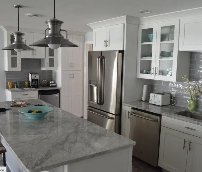 White kitchen with stainless steel appliances, gray countertops, island, and pendant lights.