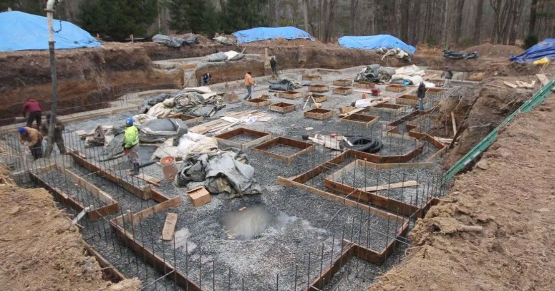 Construction site with a concrete foundation being poured; workers and equipment are visible.