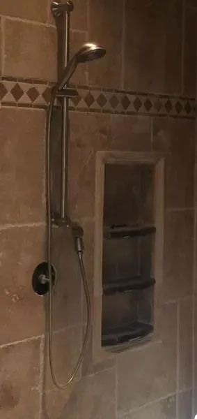 Shower with a hand shower, recessed shelves, and decorative tile accents.