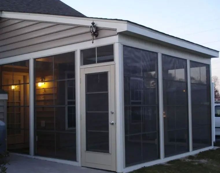 Screened-in porch attached to a house with beige siding and a door; dusk setting.