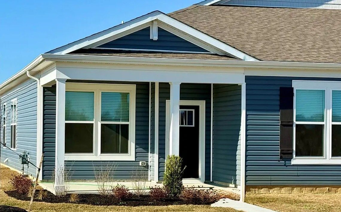 Blue-sided house with white trim, a covered porch, and black front door against a clear blue sky.