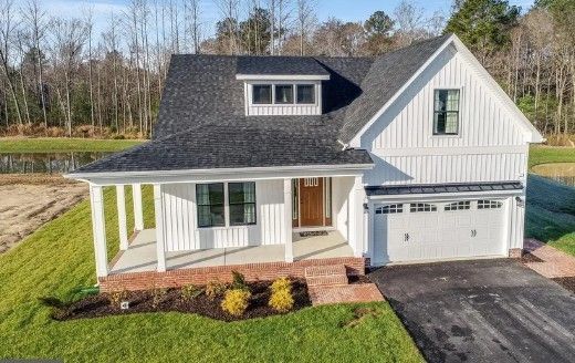 White farmhouse with black roof and a two-car garage, set in a suburban area with green grass.