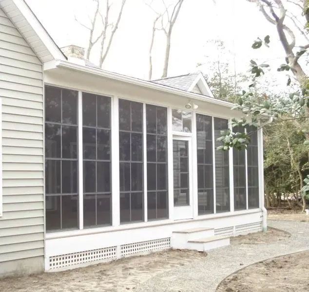 Screened porch with white trim, door, and stairs attached to a light gray house.