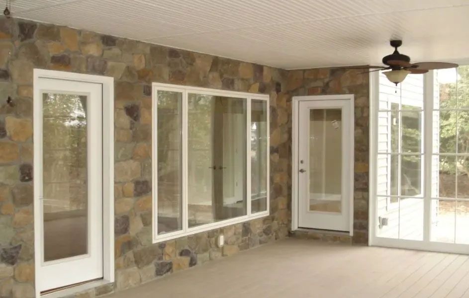 Sunroom with stone walls, multiple white-framed windows and doors, a ceiling fan, and a light-colored floor.