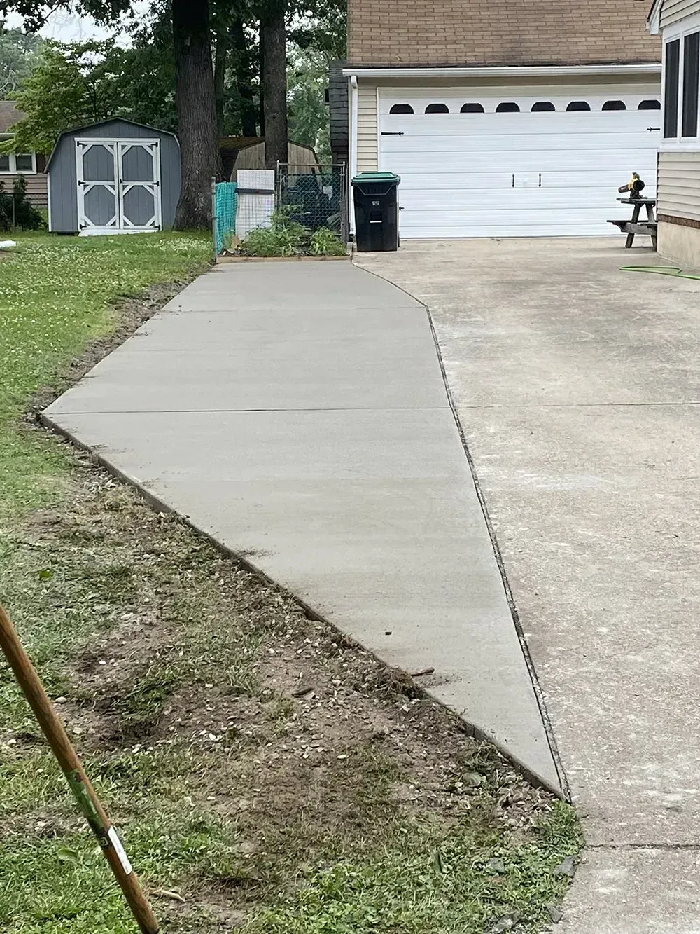 Concrete walkway leading to a garage, with a storage shed and grassy yard beside it.