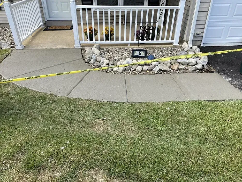 Front walkway beside a porch, with yellow caution tape and a small floodlight on a stone border.