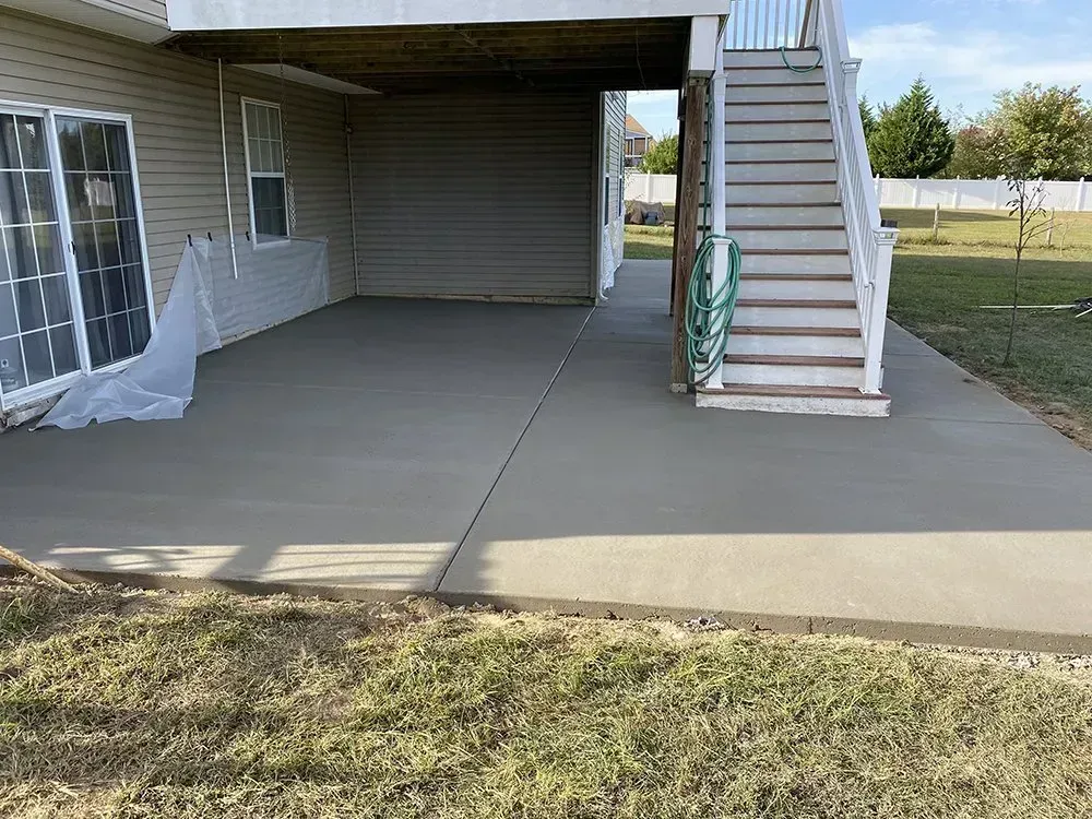 Covered concrete patio with stairs, a door, and a green hose beside a grassy yard.