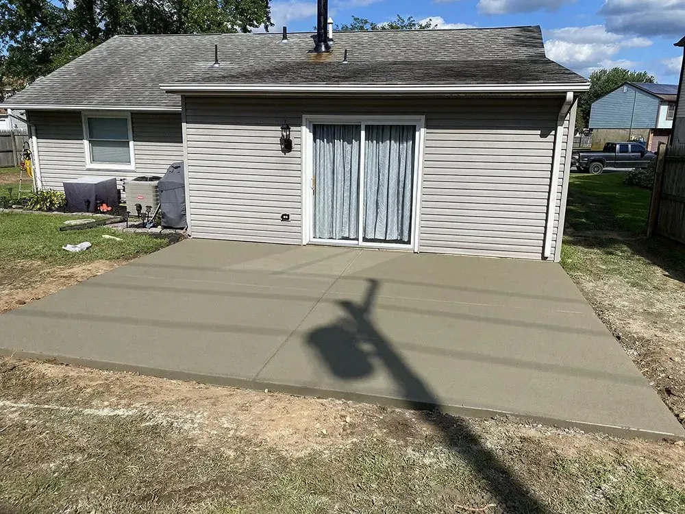 Backyard concrete patio pad in front of a house with sliding glass doors