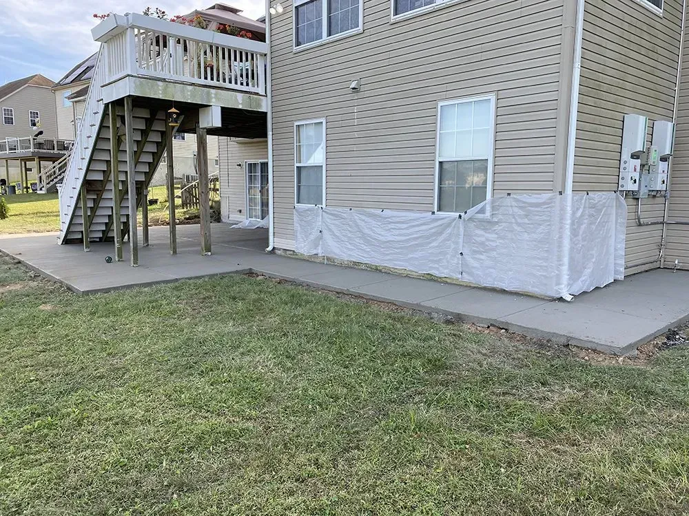 Backyard with raised deck stairs, concrete patio, and white protective barrier around house foundation