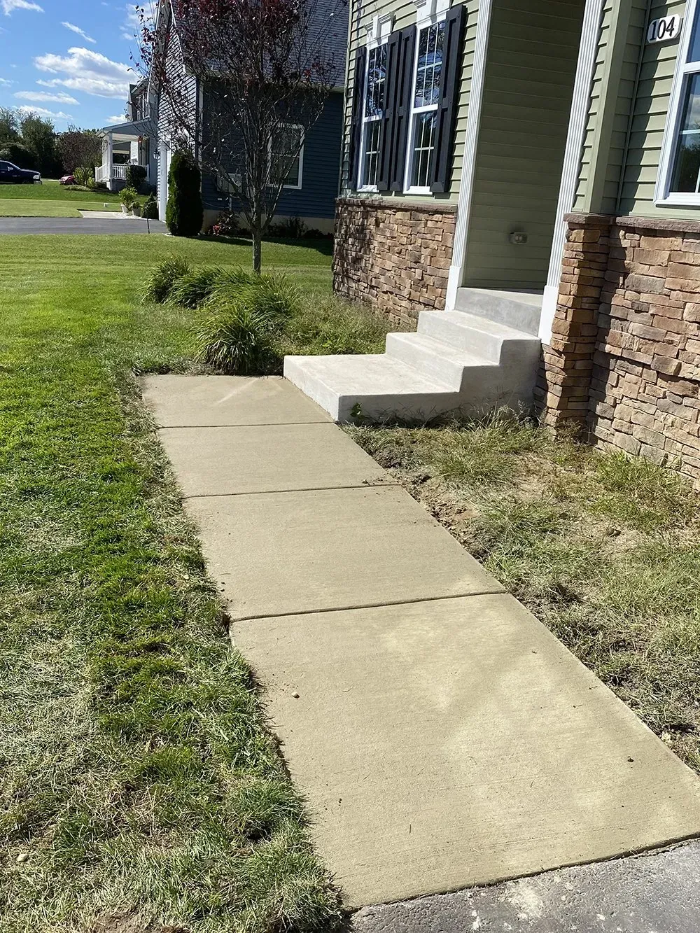 Concrete sidewalk leading to a house entrance with steps and stone siding on a sunny day