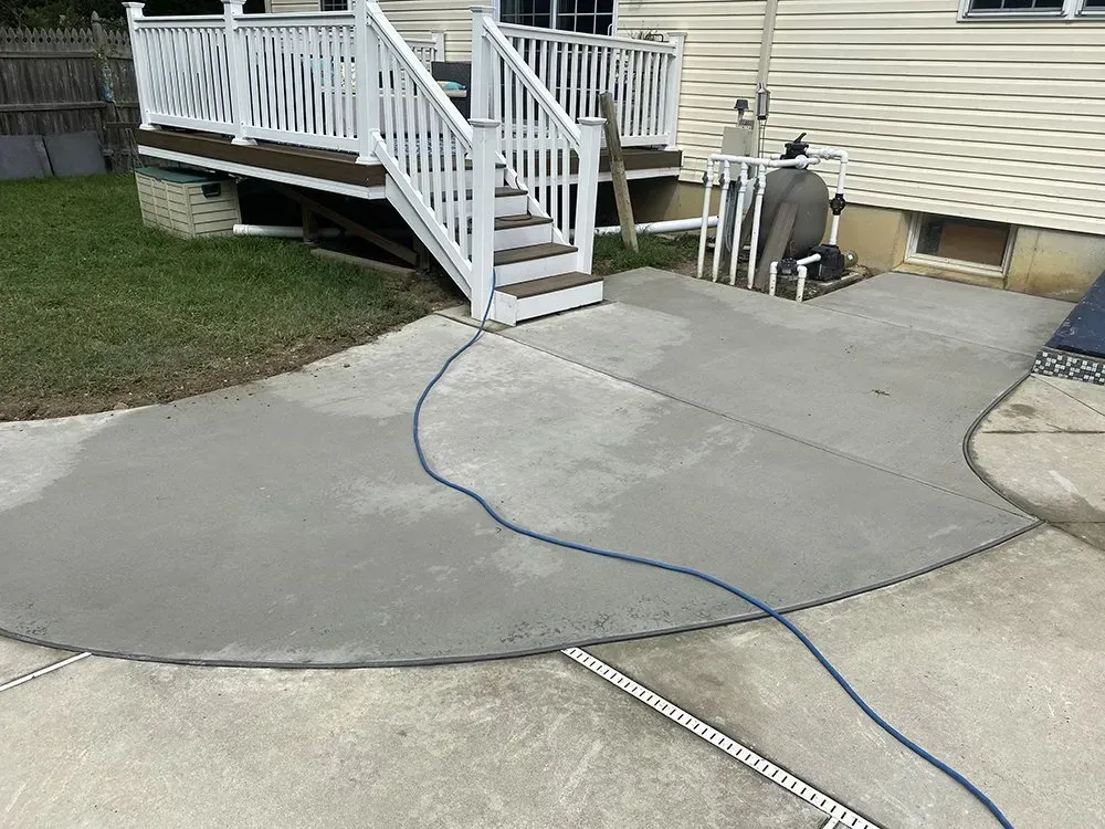 Concrete patio with a blue hose leading to white deck stairs beside a beige house