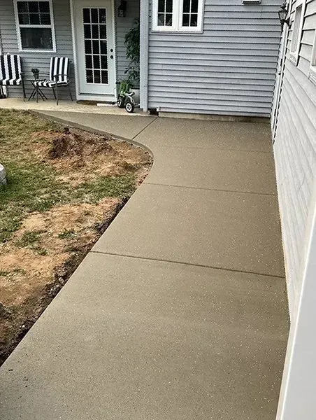 Concrete walkway beside a house, with a curved edge and patchy grass on the left.