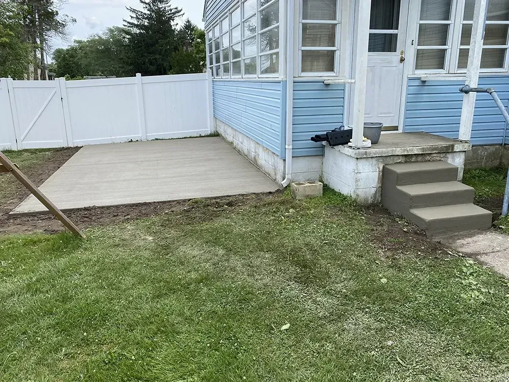 Backyard patio beside a blue house with white fence, concrete steps, and grass lawn