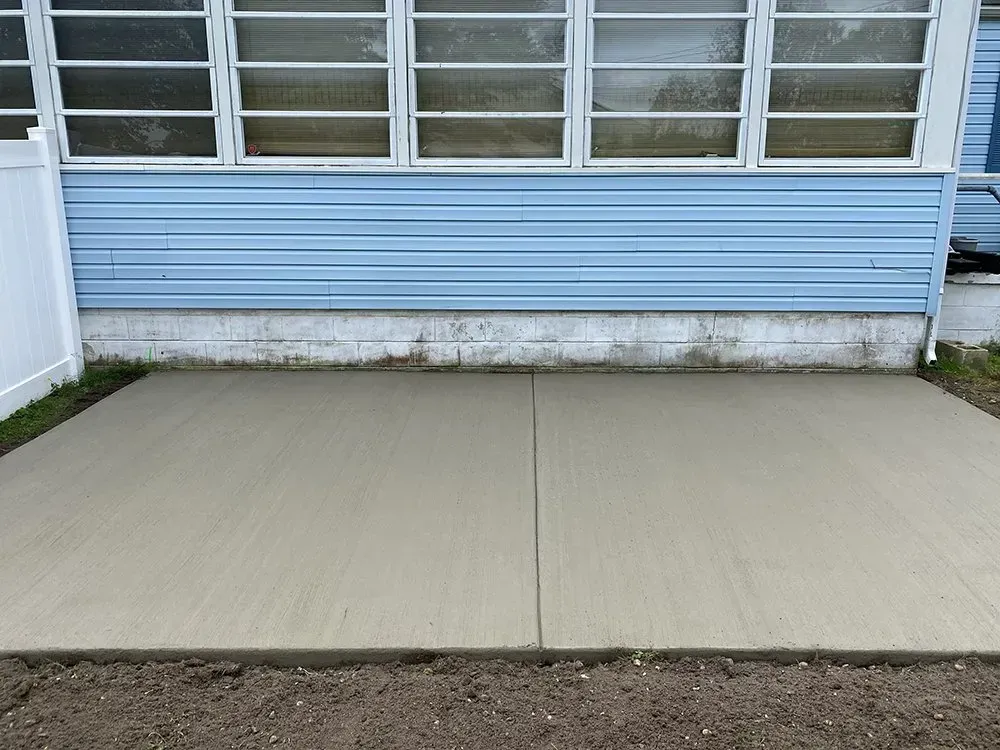Concrete patio slab in front of a blue house with a window and white siding base
