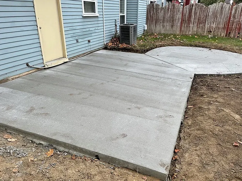 New concrete patio beside a blue house, with a curved extension and bare dirt edge