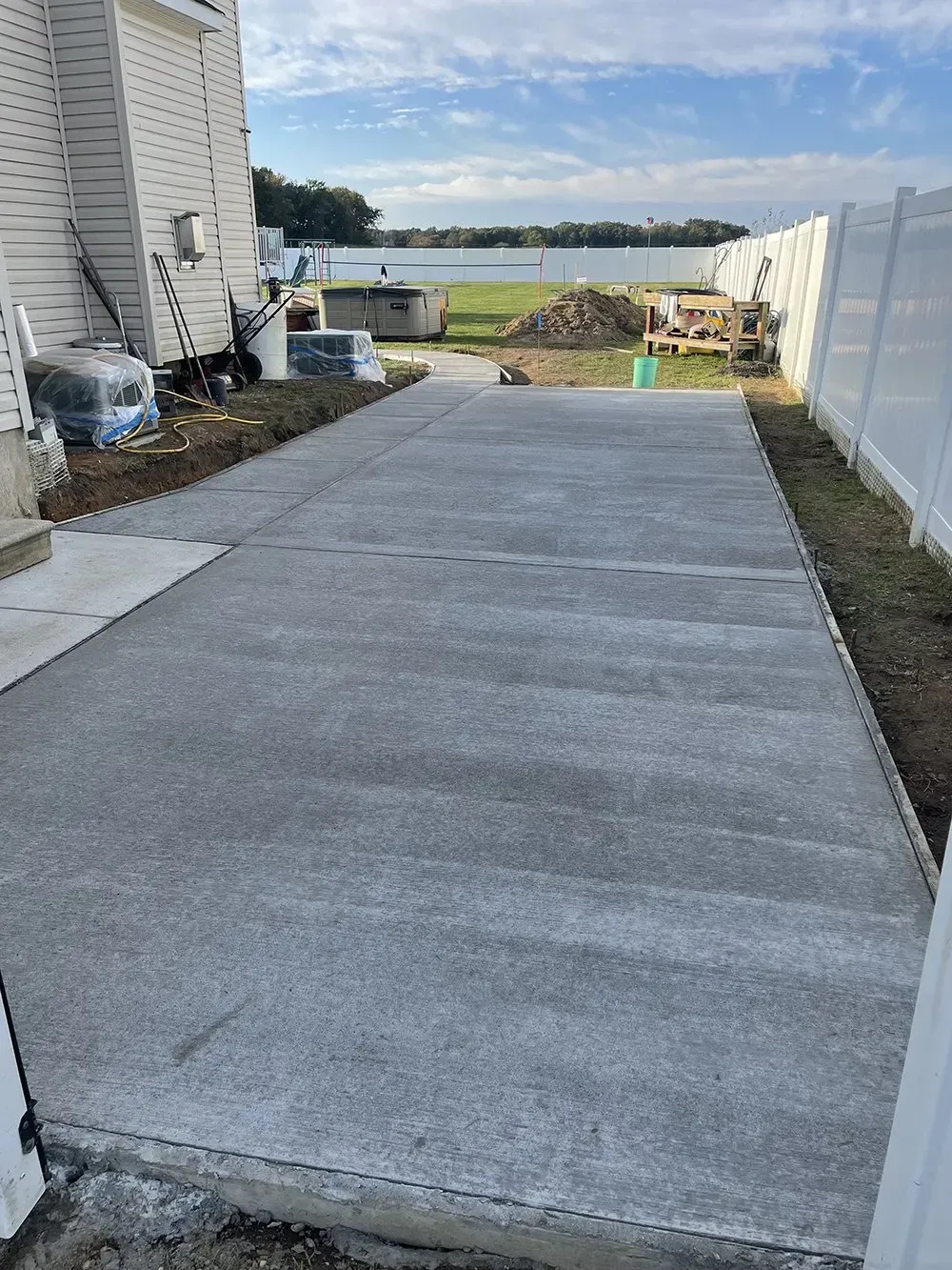 New concrete patio or walkway beside a house, leading to a fenced yard and water view.