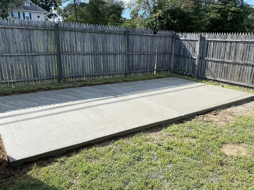Empty backyard with a smooth concrete slab and wooden privacy fence under sunlight