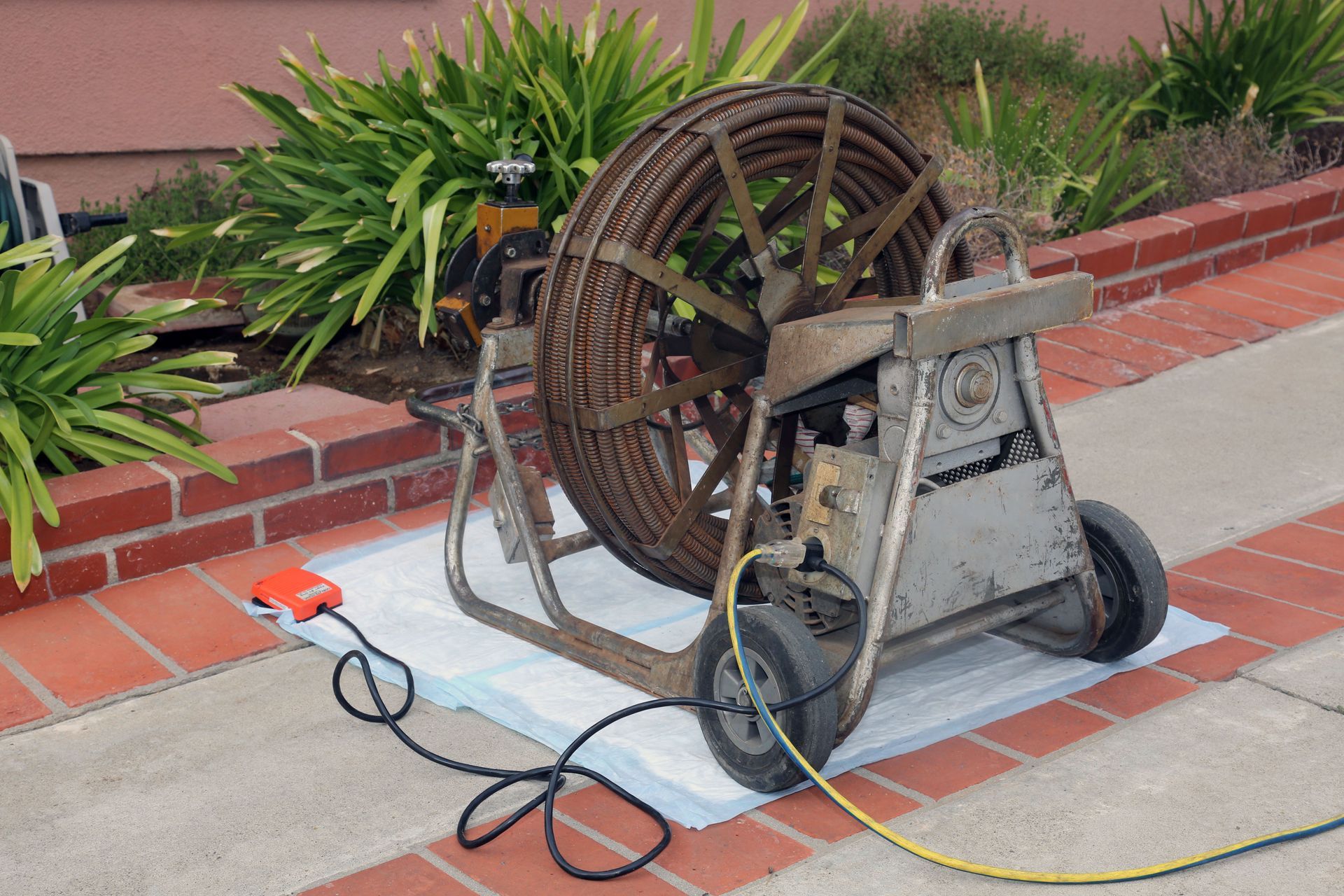 Sewer snake machine on a brick patio, ready for use, near a bush.