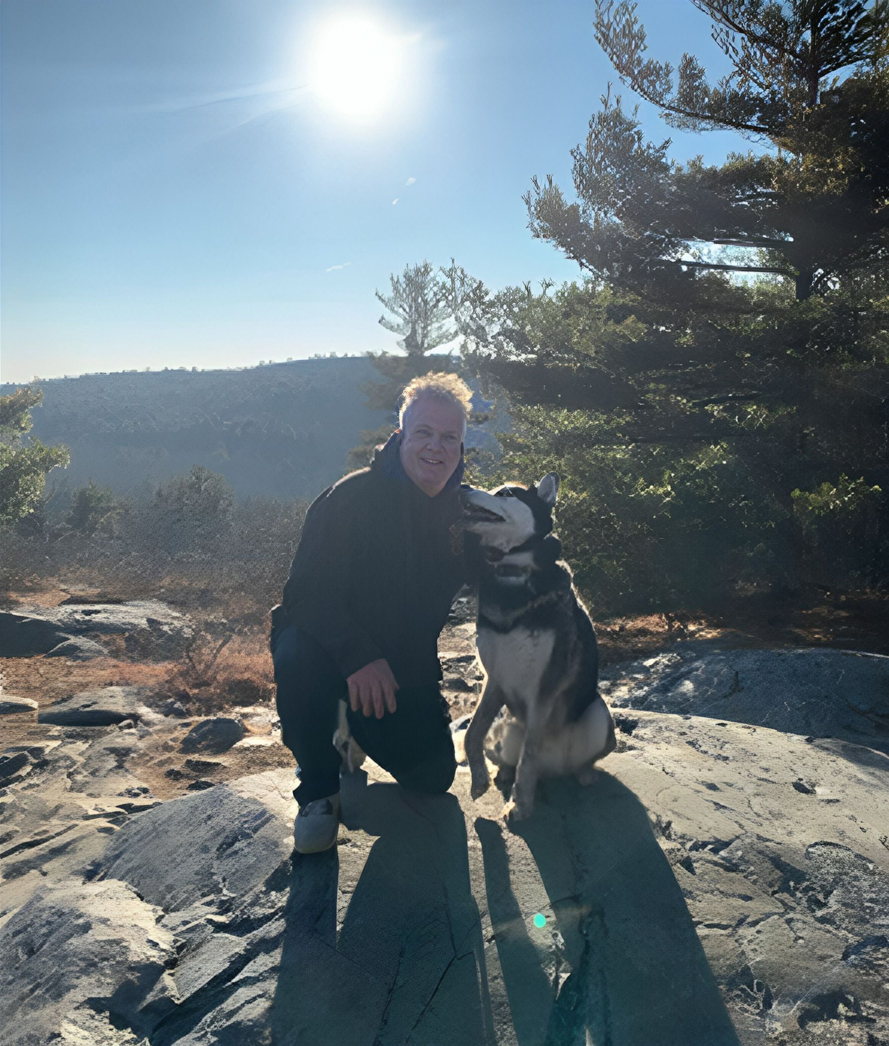 A man kneeling next to a dog on a rock