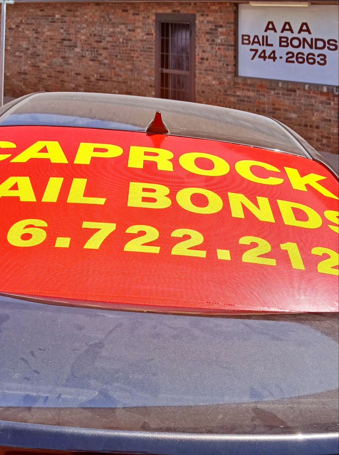 Red sign on car with CAPROCK BAIL BONDS and phone number; building in background.