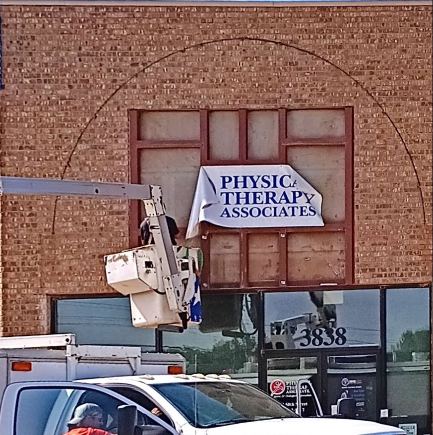 A sign for Physical Therapy Associates being installed on a brick building.