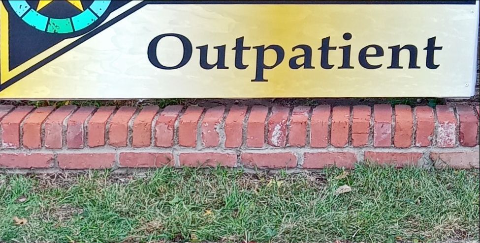 Outpatient sign above a brick wall and grass.