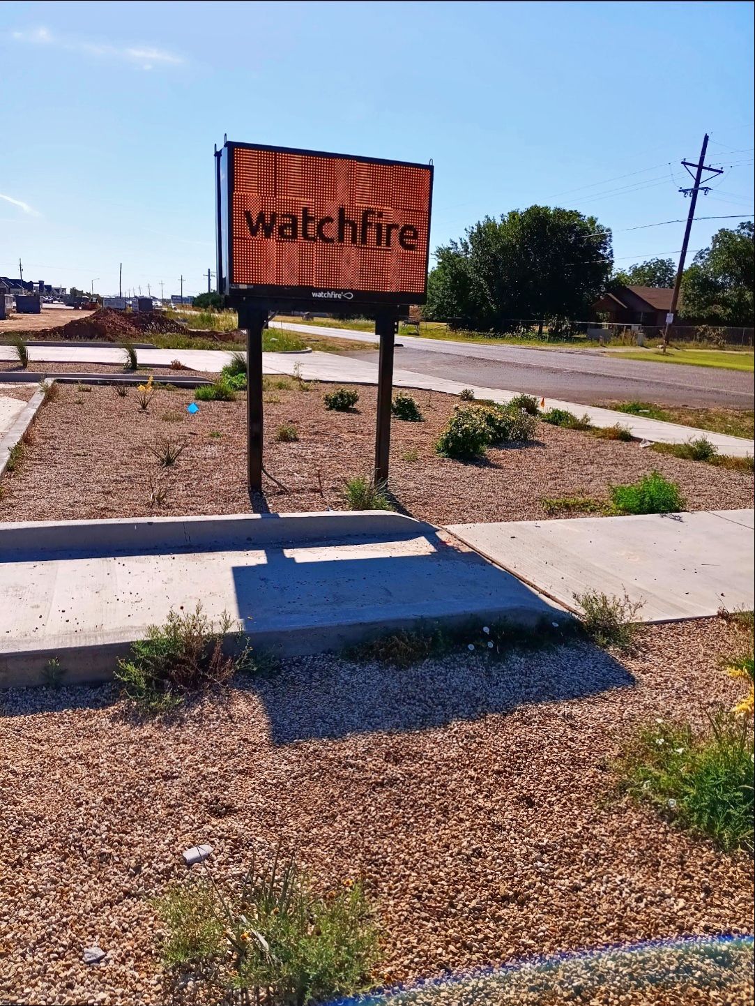 Sign for WatchFire, set in a rocky patch next to a sidewalk and a road.
