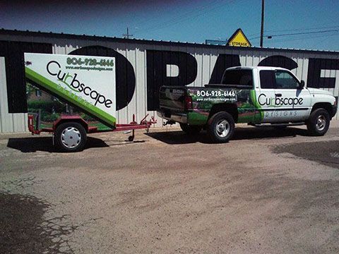 A truck and trailer are parked in front of a building that says curbscape