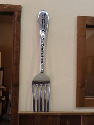 A large silver fork is hanging on a wall
