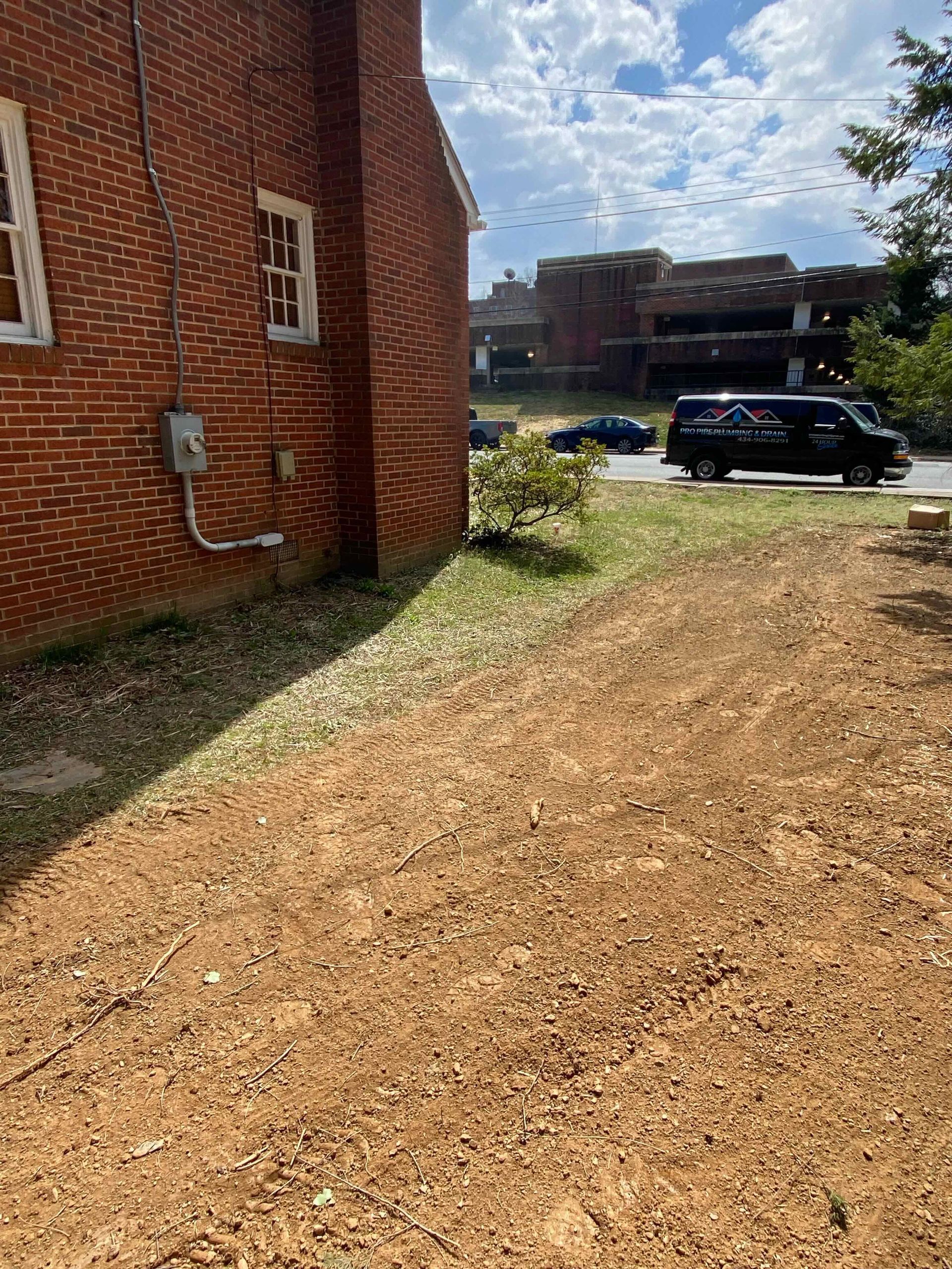 A dirt road leading to a brick building with a van parked in front of it.