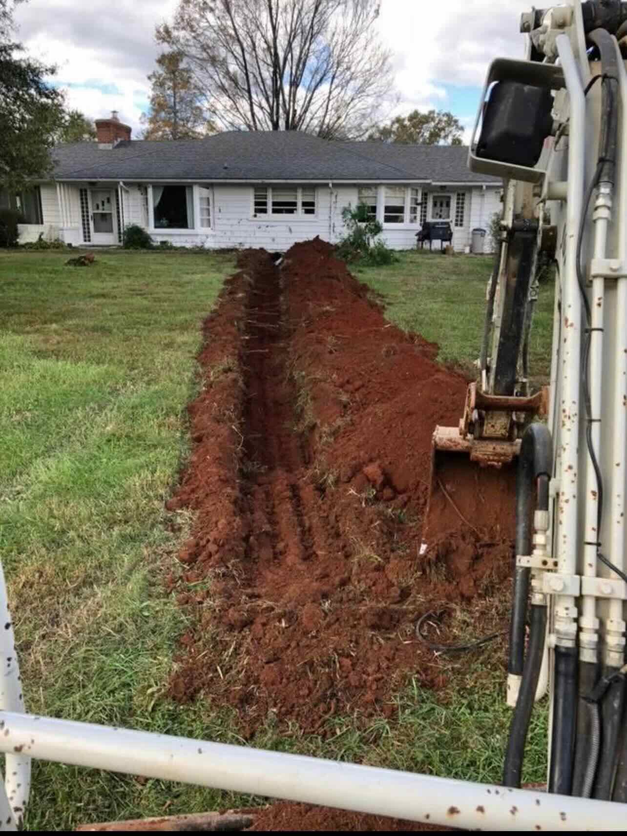 A machine is digging a trench in front of a house.