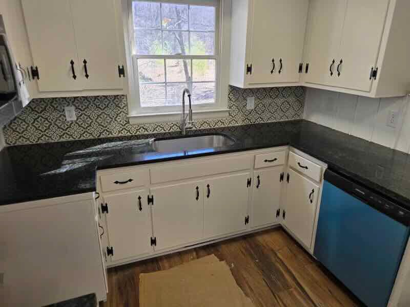 A kitchen with white cabinets , black counter tops , and a blue dishwasher.
