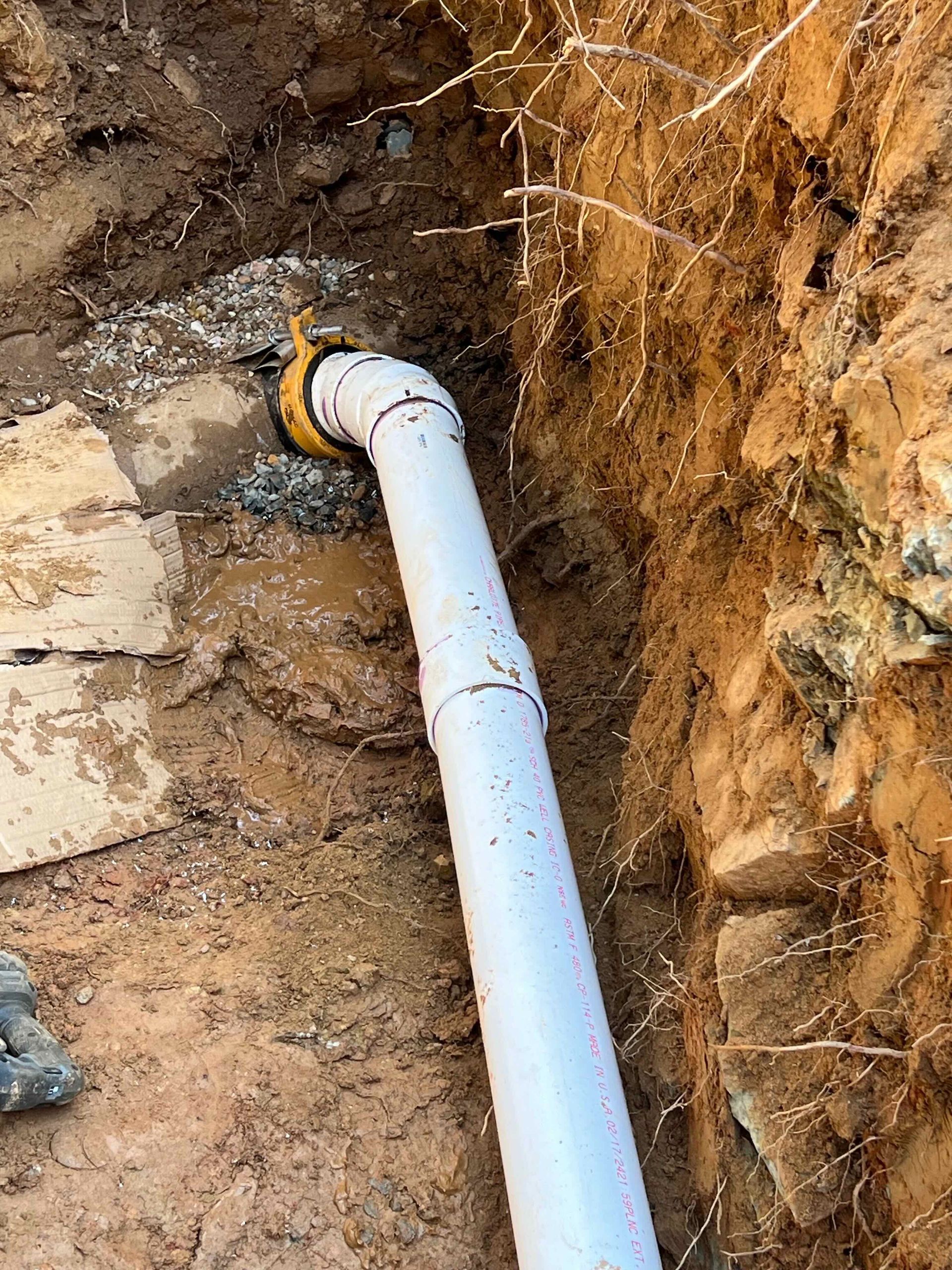 A white pipe is sitting in the dirt next to a rock wall.