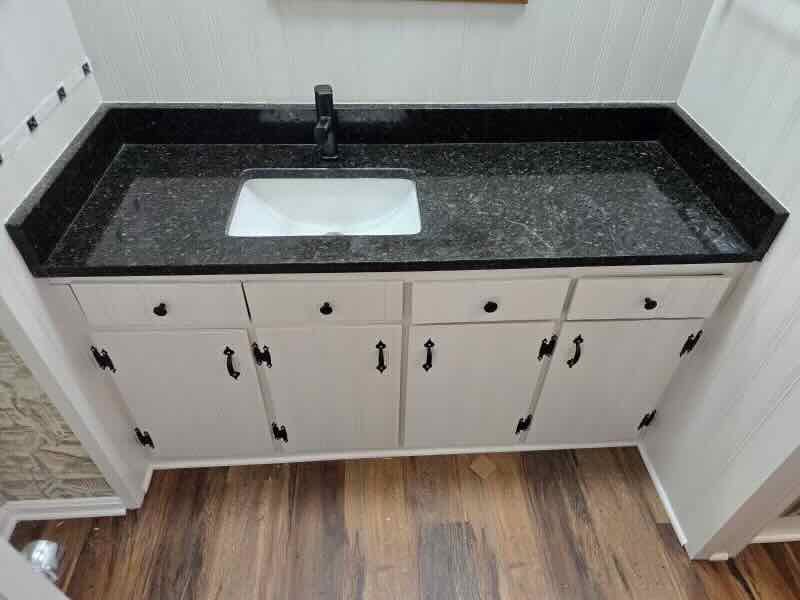 A bathroom sink with a black counter top and white cabinets.