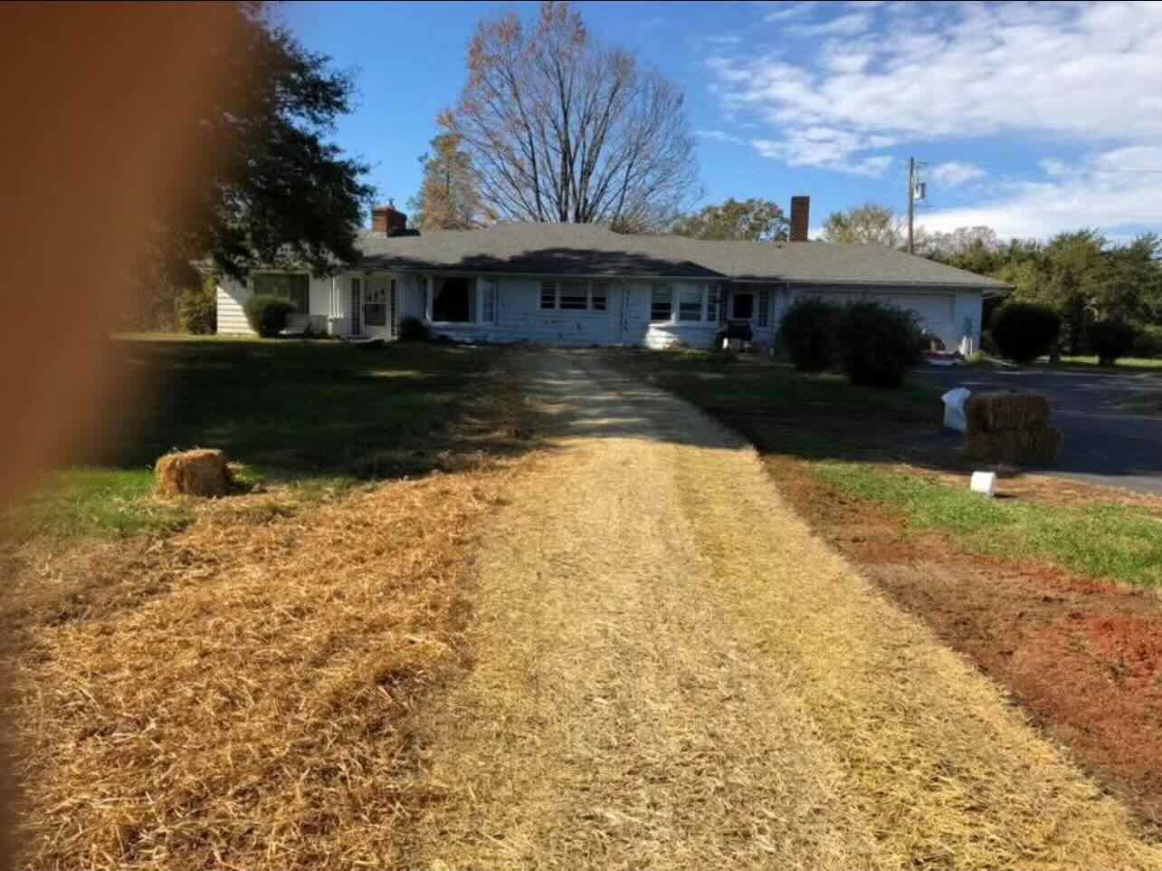 A dirt road leading to a house with hay bales on the side of it.