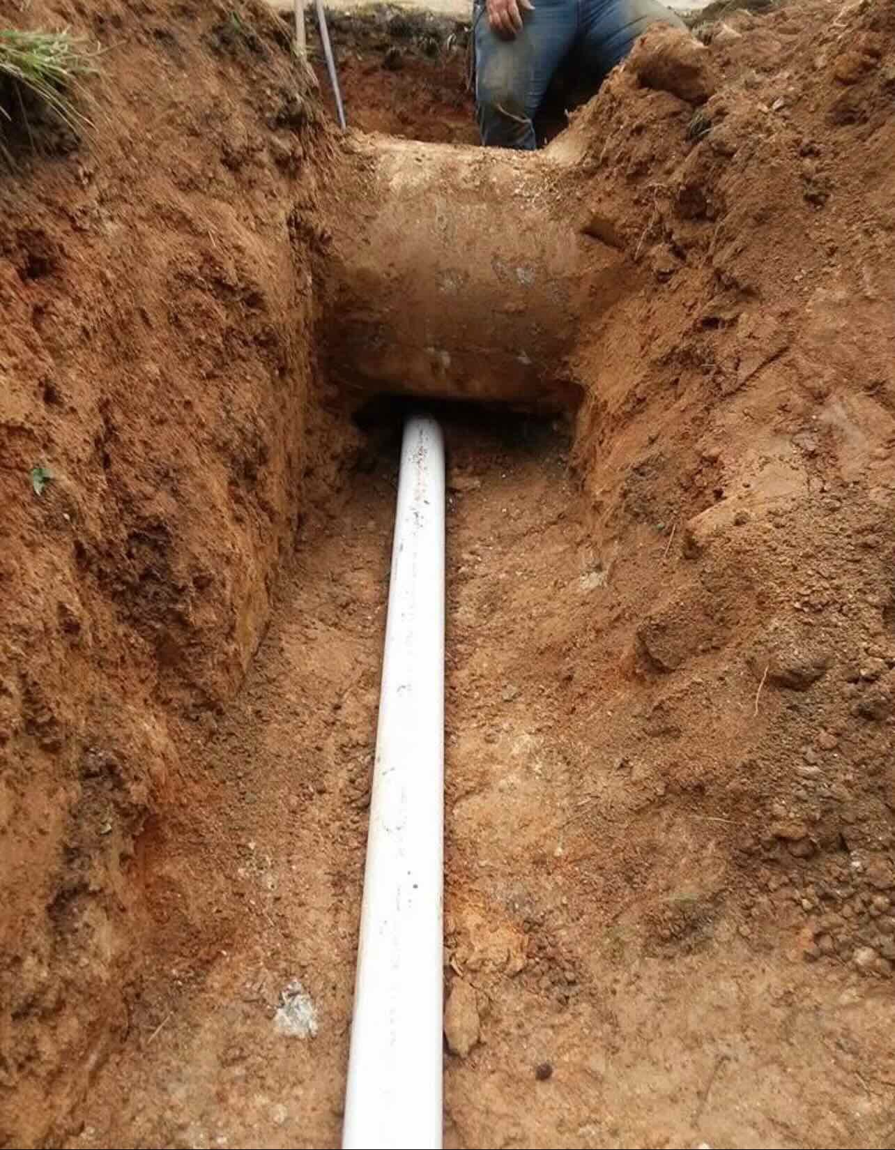 A man is digging a hole in the ground to install a pipe.