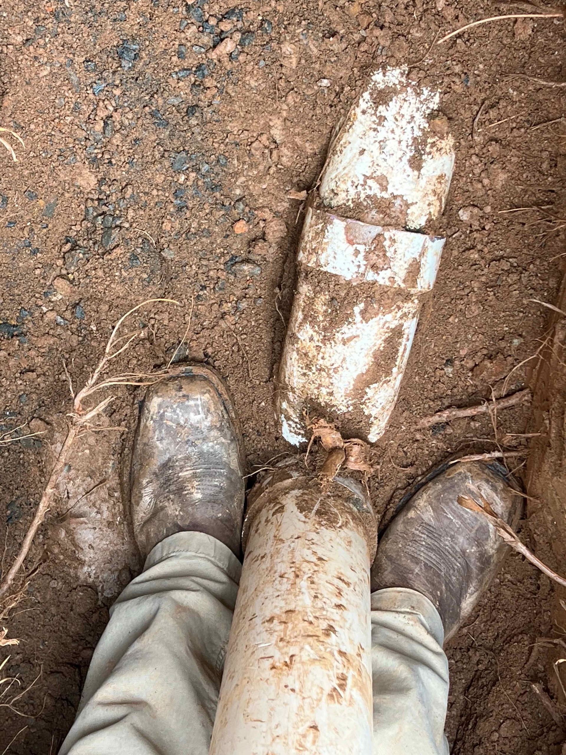 A person is standing next to a muddy object in the dirt.