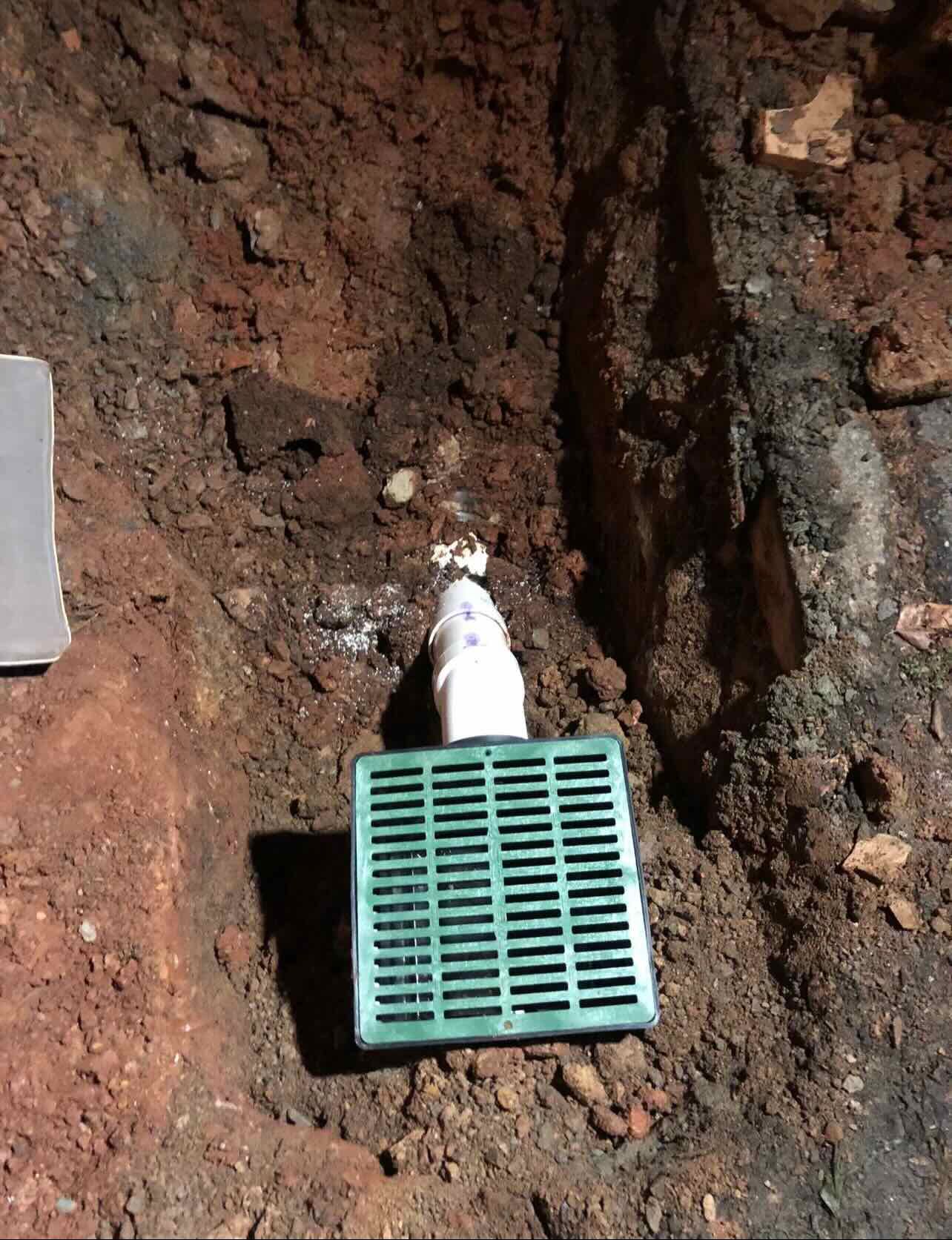 A green drain is sitting in the dirt next to a pipe.