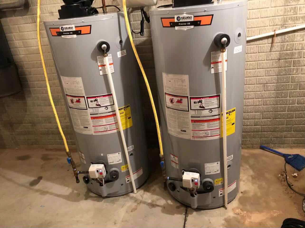 Two water heaters are sitting next to each other in a basement.
